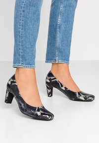 Černobílé vzorované vysoké podpatky s lesklou hadí texturou, zaoblenou špičkou a robustními blokovými podpatky.