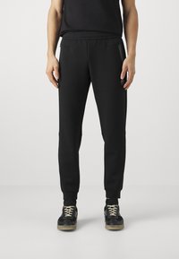 Svarta tapered sweatpants med en mjuk textur, elastisk midja, sidofickor med dragkedja och ribbad mudd, bärs med svarta sneakers.
