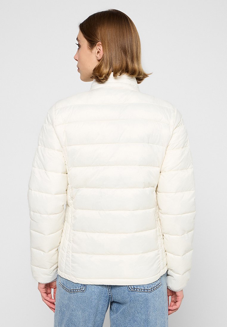 Giacca puffa bianca con motivo a righe orizzontali, colletto alto e tessuto morbido, abbinata a jeans azzurri chiari.