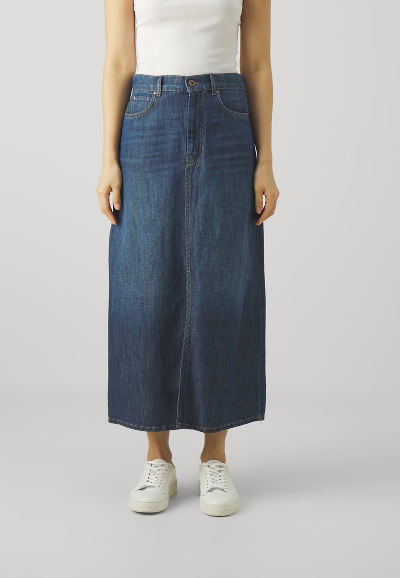 Gonna maxi in denim blu scuro, con vita alta, chiusura anteriore con bottoni e tasche laterali. Abbinata a sneakers bianche.