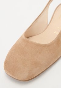 Suede slip-on shoe in light beige with a rounded toe and cutout sides, featuring a smooth interior and a flat sole.