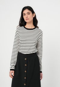 Μακρυμάνικη μπλούζα με ασπρόμαυρες ρίγες και στρογγυλή λαιμόκοψη, συνδυασμένη με μαύρη φούστα με κουμπιά μπροστά και υφή υφάσματος.