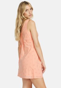 Light pink sleeveless dress with floral eyelet design, cinched waist, and ties at the back. Smooth fabric with a relaxed fit.