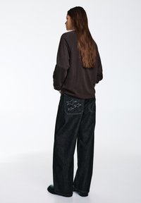 Camicia marrone a maniche lunghe con maniche raglan abbinata a jeans a gamba larga in denim scuro con ricami a forma di stella sulle tasche posteriori.