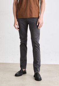 Szürke, slim fit pamutszárú nadrág, sima textúrával és klasszikus öt zsebes kialakítással. Fekete slip-on cipőkkel viselve.