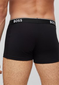 Black boxer briefs with a fitted design, featuring a soft waistband labeled "BOSS" in white lettering. Smooth texture, mid-thigh length.