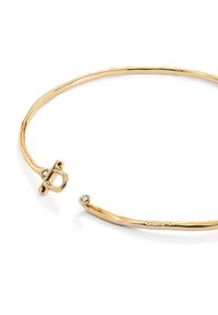 Pulsera de metal en tono dorado con un diseño liso y retorcido. Presenta un cierre de toggle circular y un pequeño acento de gema clara incrustada.