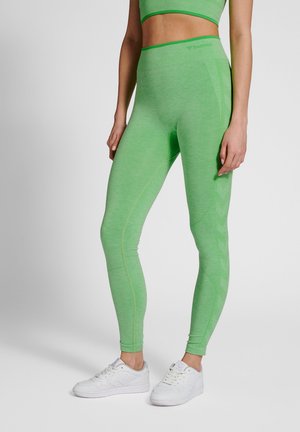 Green leggings made of a textured, stretchy fabric with a high waistband and seam accents. Paired with white athletic shoes.