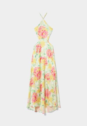 Kvinde iført en ærmeløs maxi-kjole med halterneck og pink og gult blomstret print samt cremefarvede platformsandaler med ankremmer.