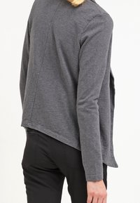 Grå långärmad topp med lös passform, med en hög-låg fåll och subtila sömnadsdetaljer. Mjukt tyg med en jämn textur.