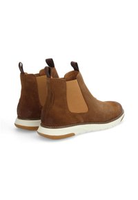 Des bottes de cheville en daim marron avec des panneaux latéraux élastiques, une languette et une semelle en caoutchouc blanche avec un profil en marron clair. Texture lisse et design épuré.