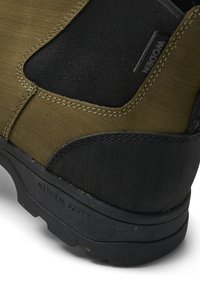 Botas verdes y negras con un acabado texturizado, parches de tela en contraste, costuras duraderas y una suela de goma resistente con un diseño de tracción.