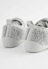 Chaussons gris avec une texture moelleuse à l'arrière, dotés d'un accent en tissu à carreaux et d'une doublure douce. La semelle est lisse et arrondie.