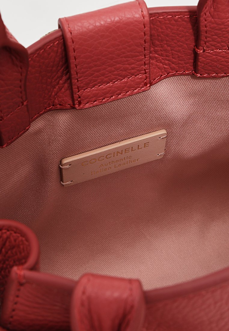 Interno di una borsa a mano in pelle rossa con rivestimento in satin liscio. Presenta un'etichetta del marchio e un materiale esterno testurizzato con cuciture visibili.