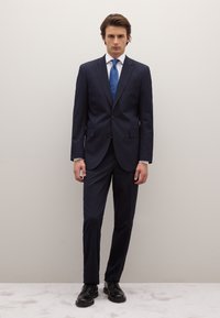 Traje azul marino de corte entallado, chaqueta de un solo pecho y dos botones. Combina con camisa blanca, corbata azul y zapatos de vestir negros.