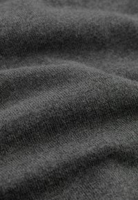 Gros plan d’un tissu tricoté gris foncé montrant une texture douce et un motif de points fins avec des plis subtils.