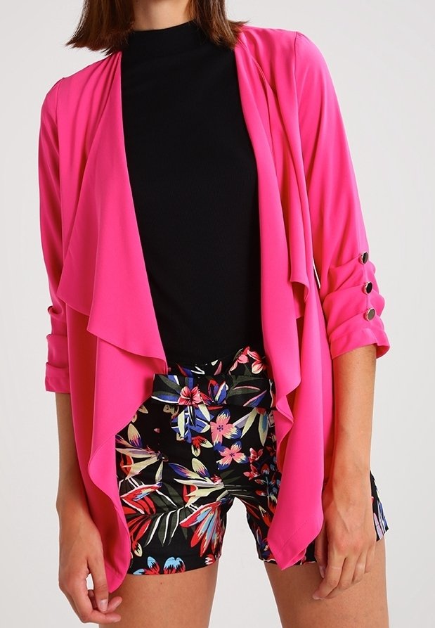 Rosa lättviktsjacka med flödande front, trekvartsärmar och rullade manschetter. Bärs över en svart topp och blommönstrade shorts.