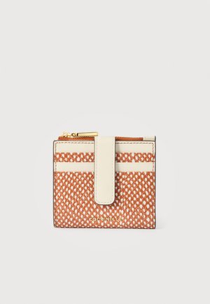 Kompakts brūns un balts rakstains maks ar krēmkrāsas siksnu un zelta rāvējslēdzēju, priekšpusē redzams zīmola nosaukums "Coccinelle".