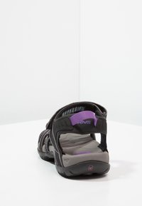 Sort og grå åben tå sandal med violet detaljer, justerbare stropper og struktureret sål, placeret på en hvid overflade mod en hvid baggrund.