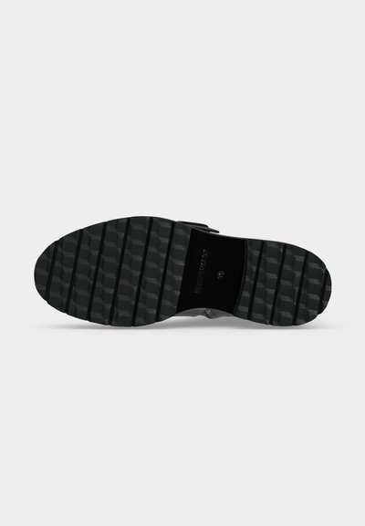 Semelle de chaussure noire avec de larges rainures horizontales et un motif texturé sur fond blanc.