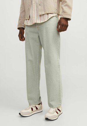 Light green denim pants with a straight cut, paired with cream sneakers featuring red accents. The outfit includes a beige jacket and striped shirt.