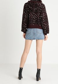 Bordeaux pullover met capuchon, voorzien van een textuurpatroon in zwart en wit. Gepaard met een lichte denim minirok en zwarte enkelboots.