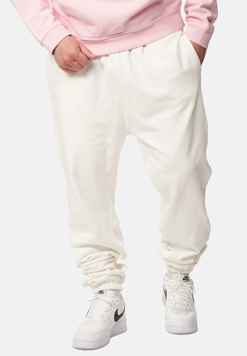 Weiße Jogginghosen mit elastischen Bündchen, aus einem weichen Stoff, kombiniert mit klassischen weißen Nike-Sneakern mit einem schwarzen Swoosh.