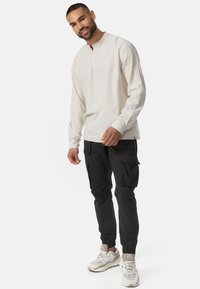 Camisa henley de manga larga en color crema con botonera frontal, combinada con pantalones cargo negros que cuentan con bolsillos laterales y puños elásticos en los tobillos.