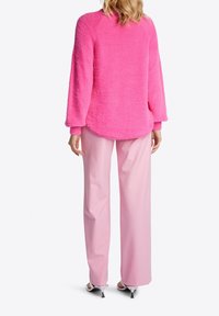 Maglione fluffy rosa con maniche lunghe e orlo arrotondato, abbinato a pantaloni ampi rosa chiaro e sandali con tacco argento.
