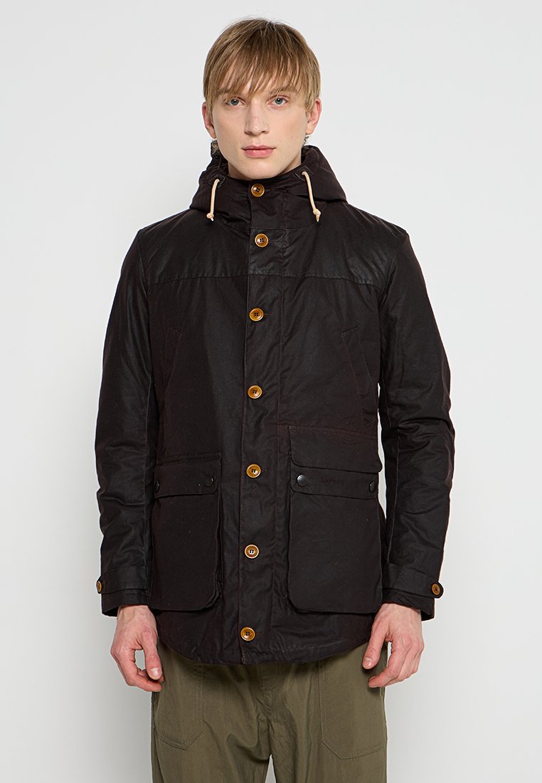 Black, waxed fabric jacket with a hood, featuring brown buttons, two front pockets, and drawstring accents. Casual design with a fitted shape.