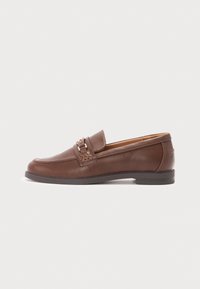 Mocasín de cuero marrón con suela plana, que presenta un acento decorativo de hebilla y un detalle de costura en los laterales. Textura suave y forma redondeada.