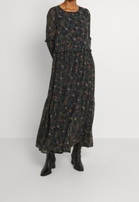 Lång, svart blommig klänning med rund halsringning, långa ärmar och volangmanchetter; har en flerlagersdesign med färgglada botaniska mönster.