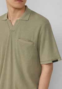 Oliwkowa, prążkowana koszulka polo z dekoltem w serek i krótkimi rękawami. Posiada naszywką kieszonkę oraz tkane etykietę na dolnym brzegu. Miękka tekstura.