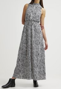 Maxi dress in black and white abstract pattern, sleeveless with high neckline, fitted waist, flowing skirt, paired with black ankle boots.