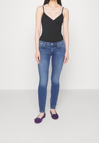 Bodysuit sin mangas negro, jeans ajustados azules y bailarinas moradas. El bodysuit tiene un diseño de escote en V, los jeans cuentan con bolsillos y un corte slim.