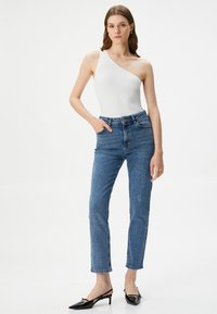 Bodysuit blanco de canalé con un hombro, combinado con vaqueros de pierna recta azul claro con detalles desgastados y tacones negros de punta.