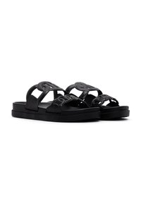 Sandalias de tiras negras con doble correa que presentan un patrón texturizado y un ligero brillo metálico. Suela plana con un acabado suave.