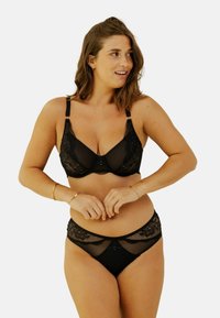 Ensemble de lingerie en dentelle noire comprenant un soutien-gorge balconnet avec des bretelles réglables et un slip assorti avec des détails en dentelle florale et des accents transparents.