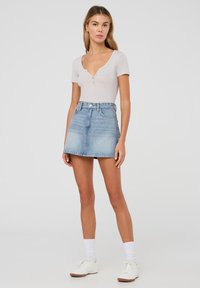 Body corto grigio chiaro a maniche corte con scollatura a V profonda e dettaglio di bottoni, abbinato a una mini gonna di jeans azzurri a vita alta. Sneakers bianche e calze.