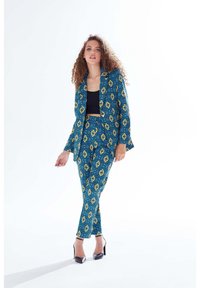 Blue and yellow patterned suit with a fitted jacket and trousers, made of textured fabric, featuring a geometric design and sharp lapels.