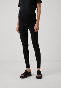 Leggings pretos de maternidade com uma cintura alta. Feitas a partir de um tecido elástico, com uma textura suave, apresentam uma silhueta ajustada.