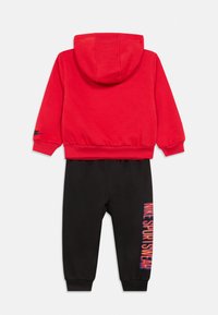 Felpa rossa con cappuccio e tasca a marsupio frontale, e pantaloni di felpa neri con una stampa verticale "NIKE SPORTSWEAR" in colori sfumati sulla gamba.