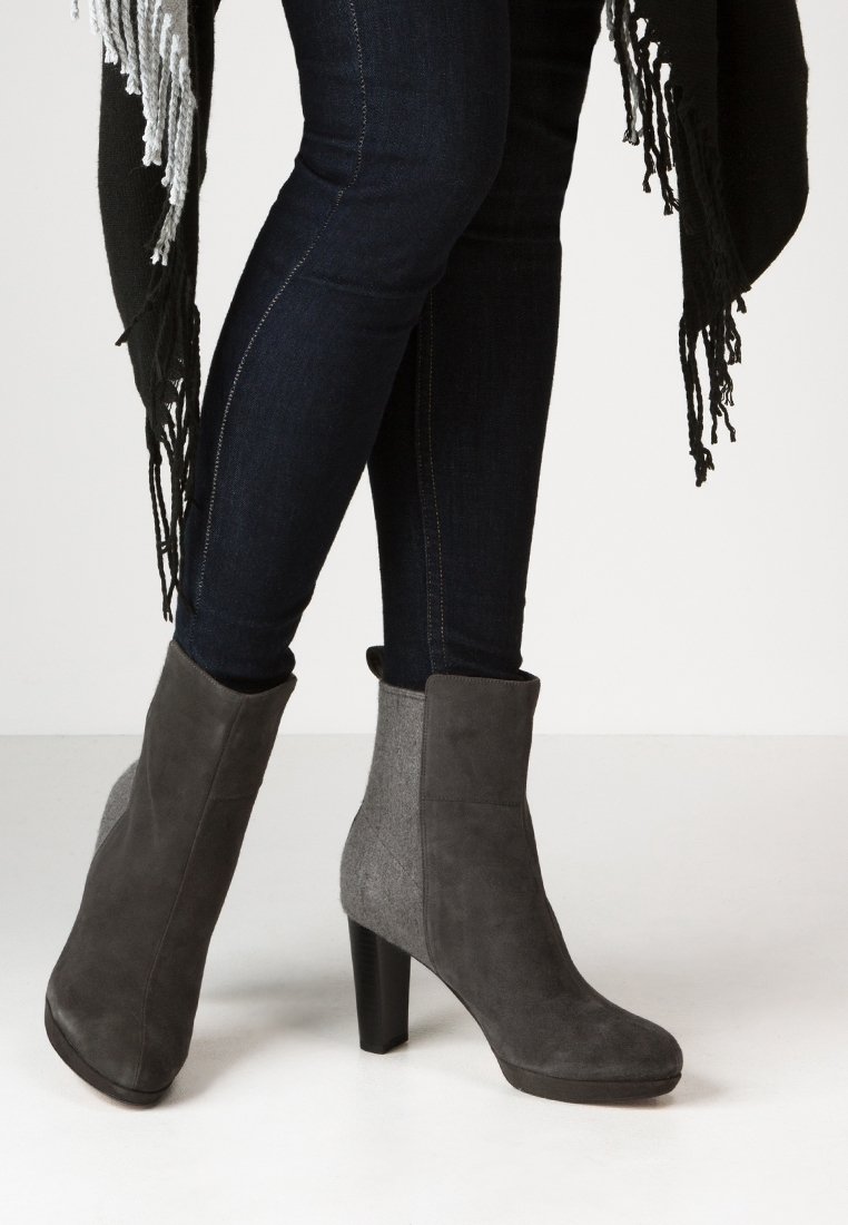 Bottes chevilles grises combinant daim et feutre, dotées d'un talon haut et d'une texture de surface lisse, portées avec un pantalon en denim foncé.