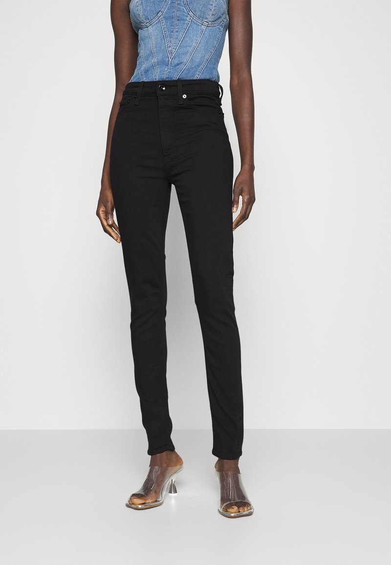Jean noir taille haute avec une coupe slim, en denim, associés à des mules transparentes à talons. L'ensemble a un design minimaliste.