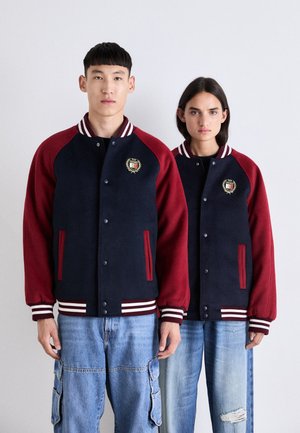 Marineblå og bordeaux varsity jakker med hvide stribede manchetter og krave. Har broderet emblem og sidelommer. Casual pasform, blødt stof.