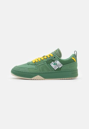 Grüner Sneaker mit niedrigem Schaft, gelben Schnürsenkeln, strukturierter Sohle, Mesh- und Lederpaneelen und einem weißen, aufgenähten Label an der Seite.