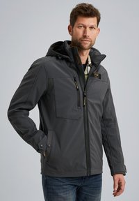 Gray waterproof jacket with a hood, featuring zippered front pockets, patches, and a textured finish. Worn over a checkered shirt.