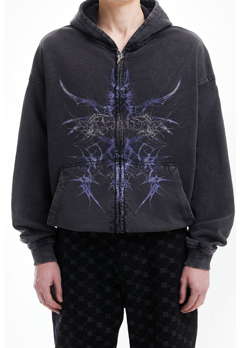 Sweat à capuche noir zippé avec un motif graphique violet présentant des pointes acérées à l'avant. Il possède une capuche à cordon et des poches frontales.