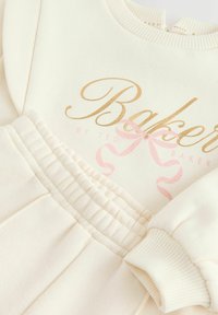 Krémový dvoudílný set z bavlny s ribovaným výstřihem, elastickým pasem a potištěným zlatým a růžovým textem s designem mašle.