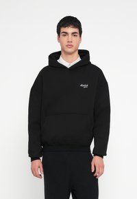Fekete kapucnis pulóver pamutból, elülső zsebbel, bordázott mandzsettákkal és bal oldalon fehér hímzett logóval.